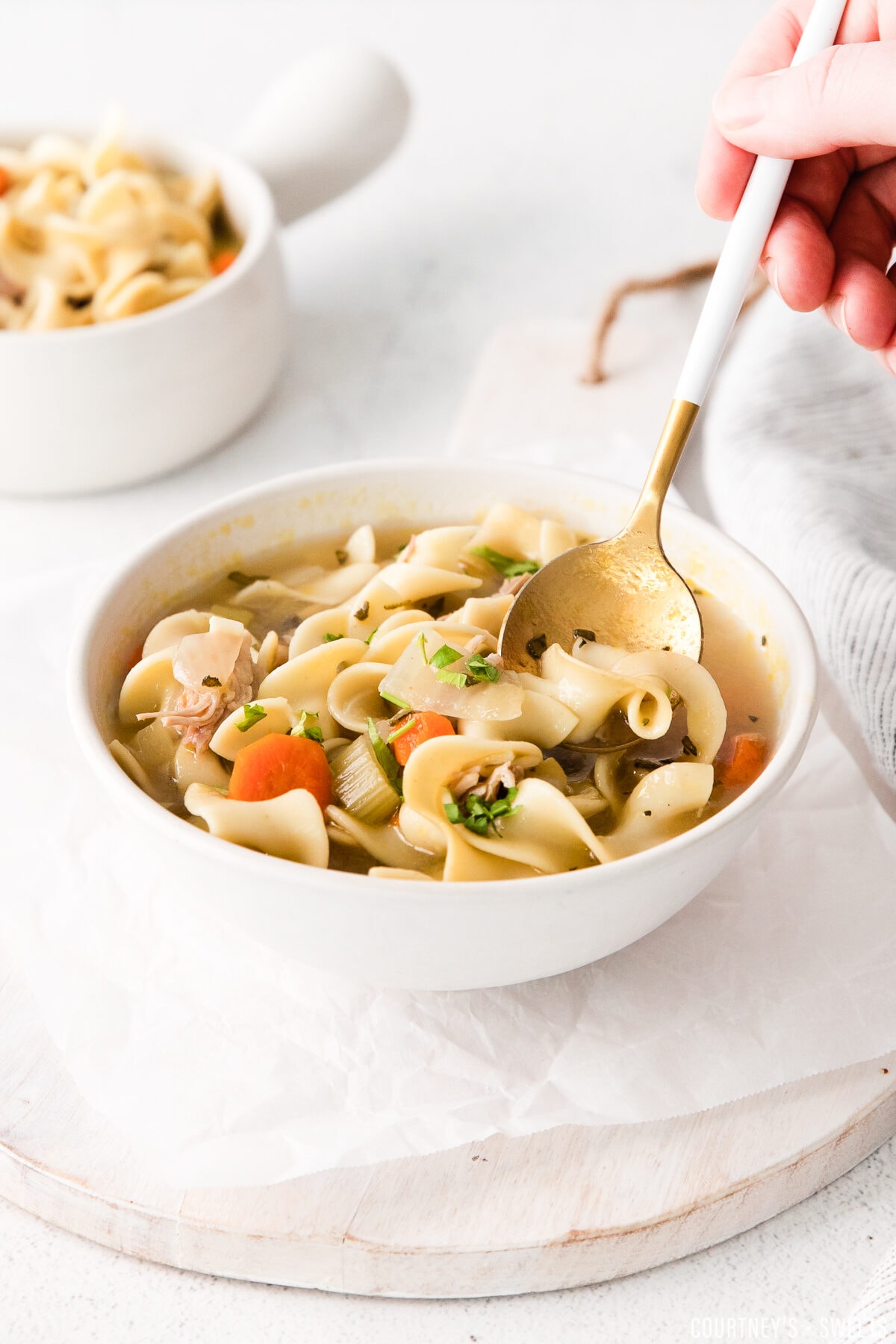 hand with spoon scooping turkey noodle soup out of a white bowl