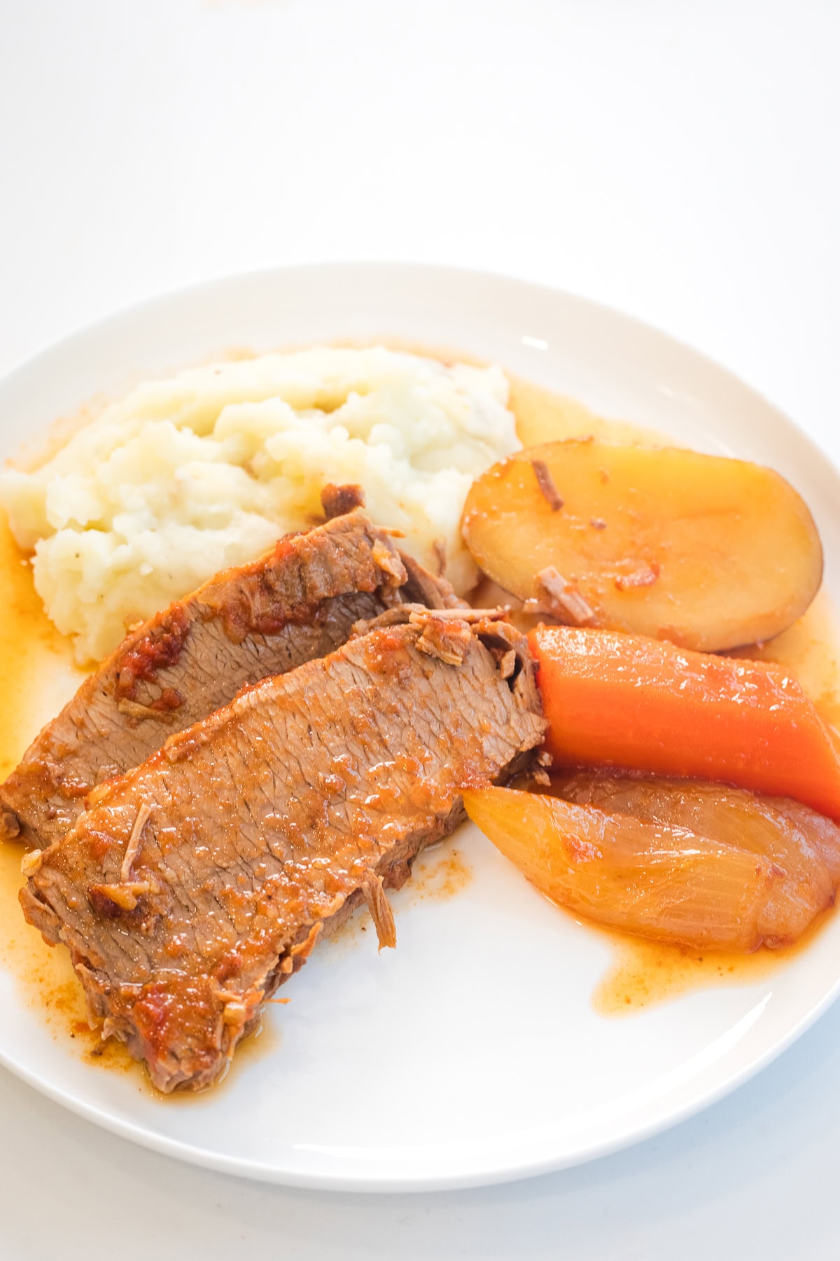 jewish brisket recipe on a plate with potatoes, carrots, onion, and mashed potatoes.