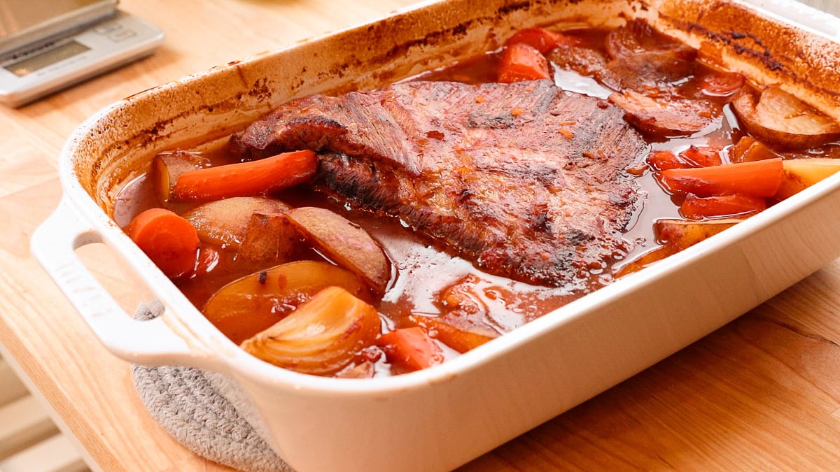 cooked jewish brisket in a casserole dish with onions, carrots and potatoes.