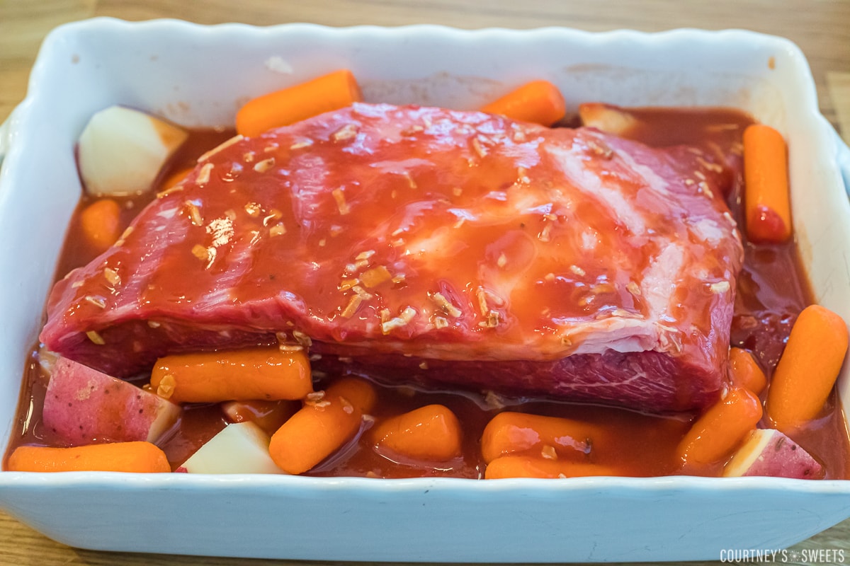 ketchup gingerale and onion soup mixture poured over top brisket over carrots and potatoes in a white casserole dish