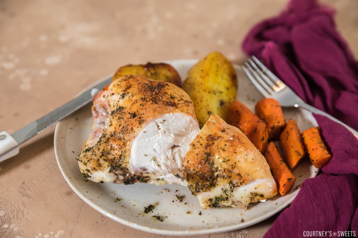 cut open roasted split chicken breast on plate with roasted carrots and potatoes