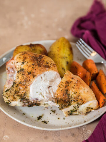 sliced open roasted split chicken breast on plate with roasted carrots and potatoes