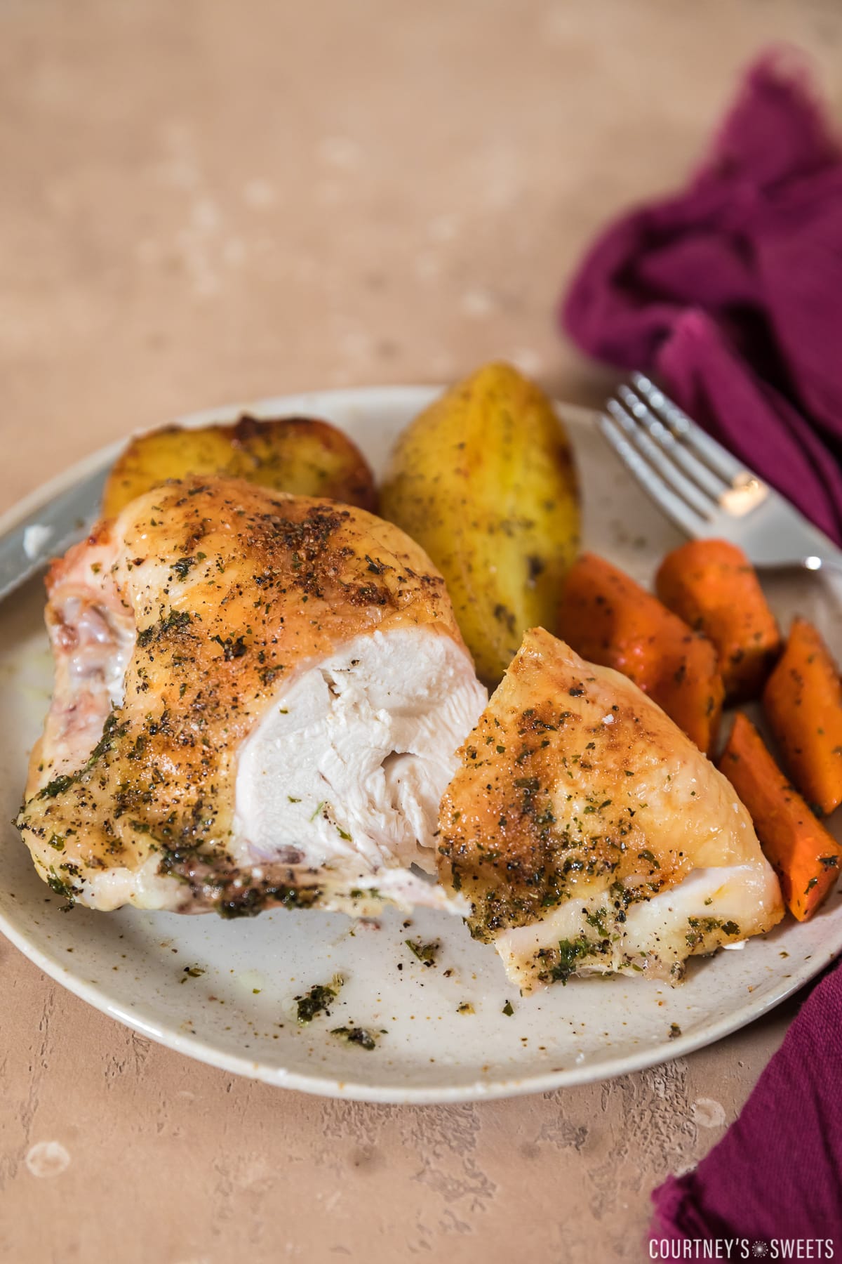 sliced open roasted split chicken breast on plate with roasted carrots and potatoes