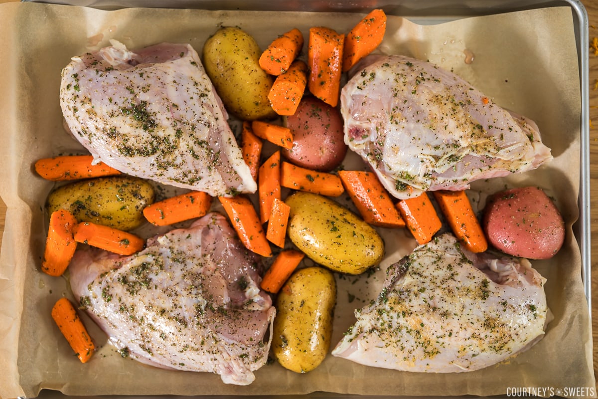 raw split chicken breasts with potatoes and carrots on a sheet pan