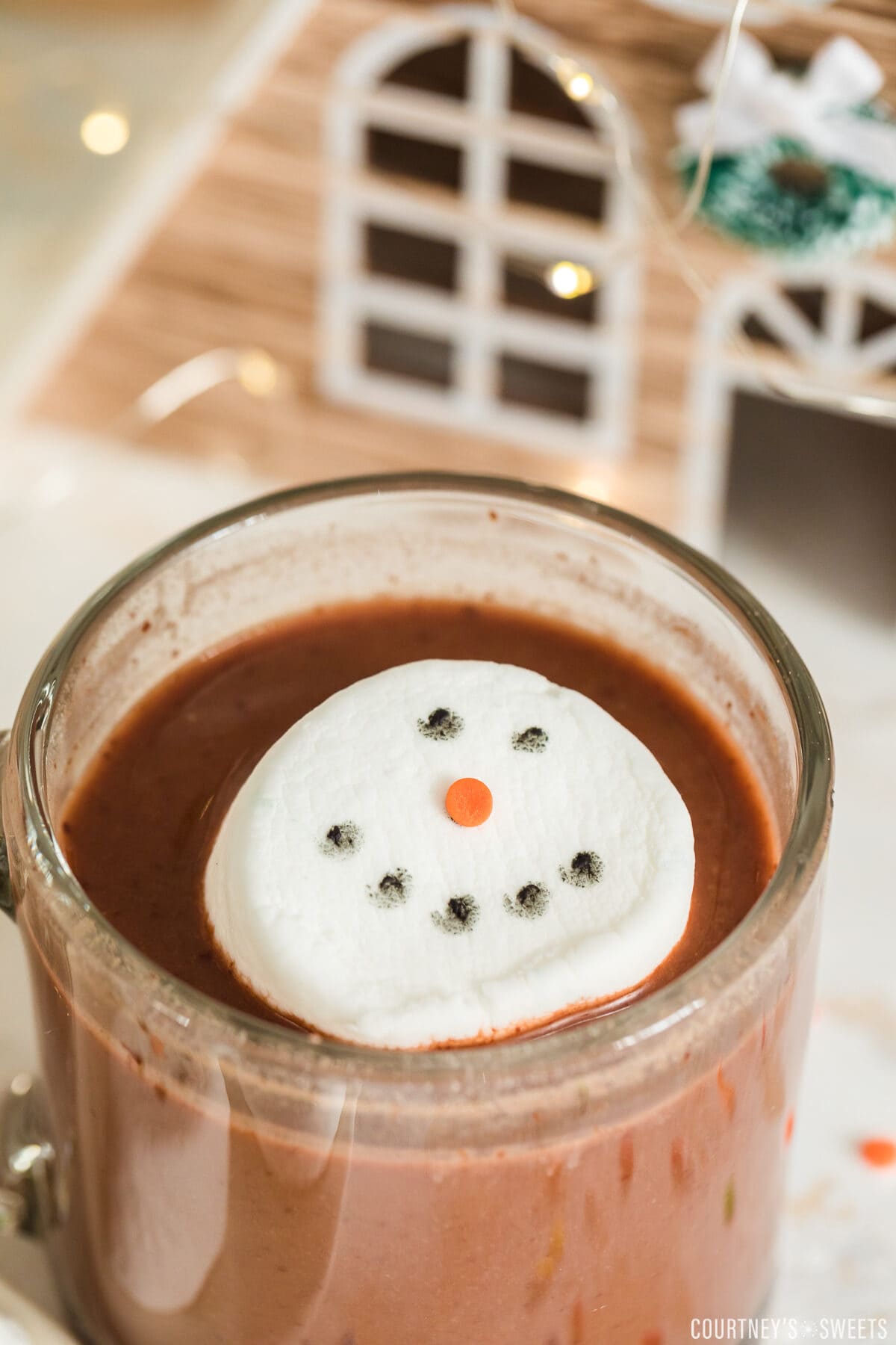 snowman hot chocolate topper floating in hot chocolate in a glass mug