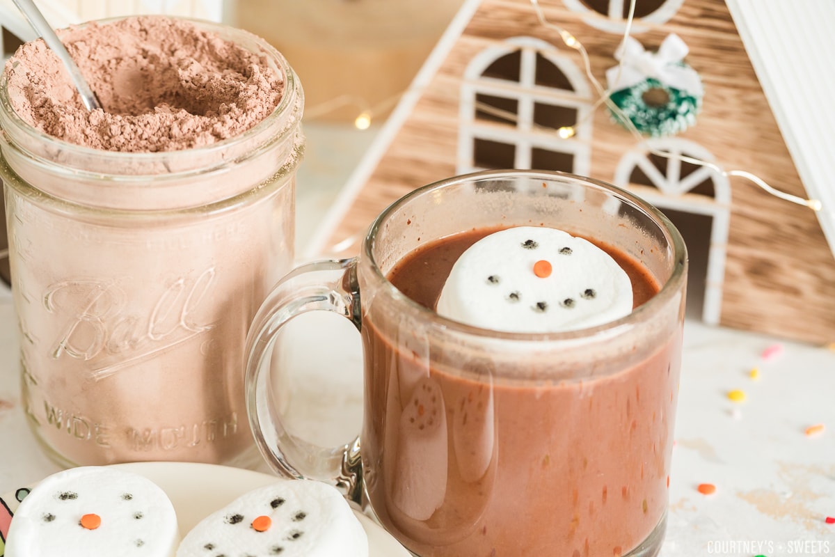 snowman hot chocolate topper floating in hot chocolate in a glass mug
