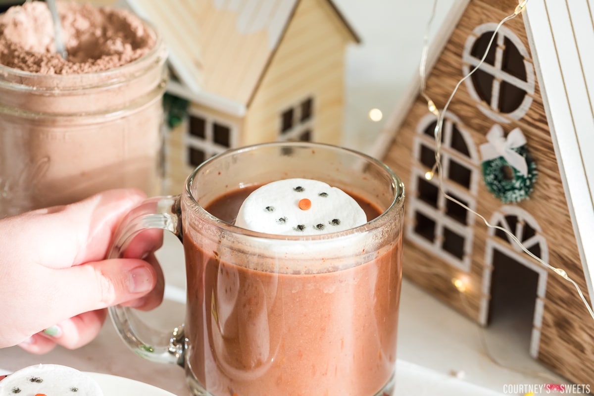 child hand holding hot chocolate mug with marshmallow snowman topper inside of it