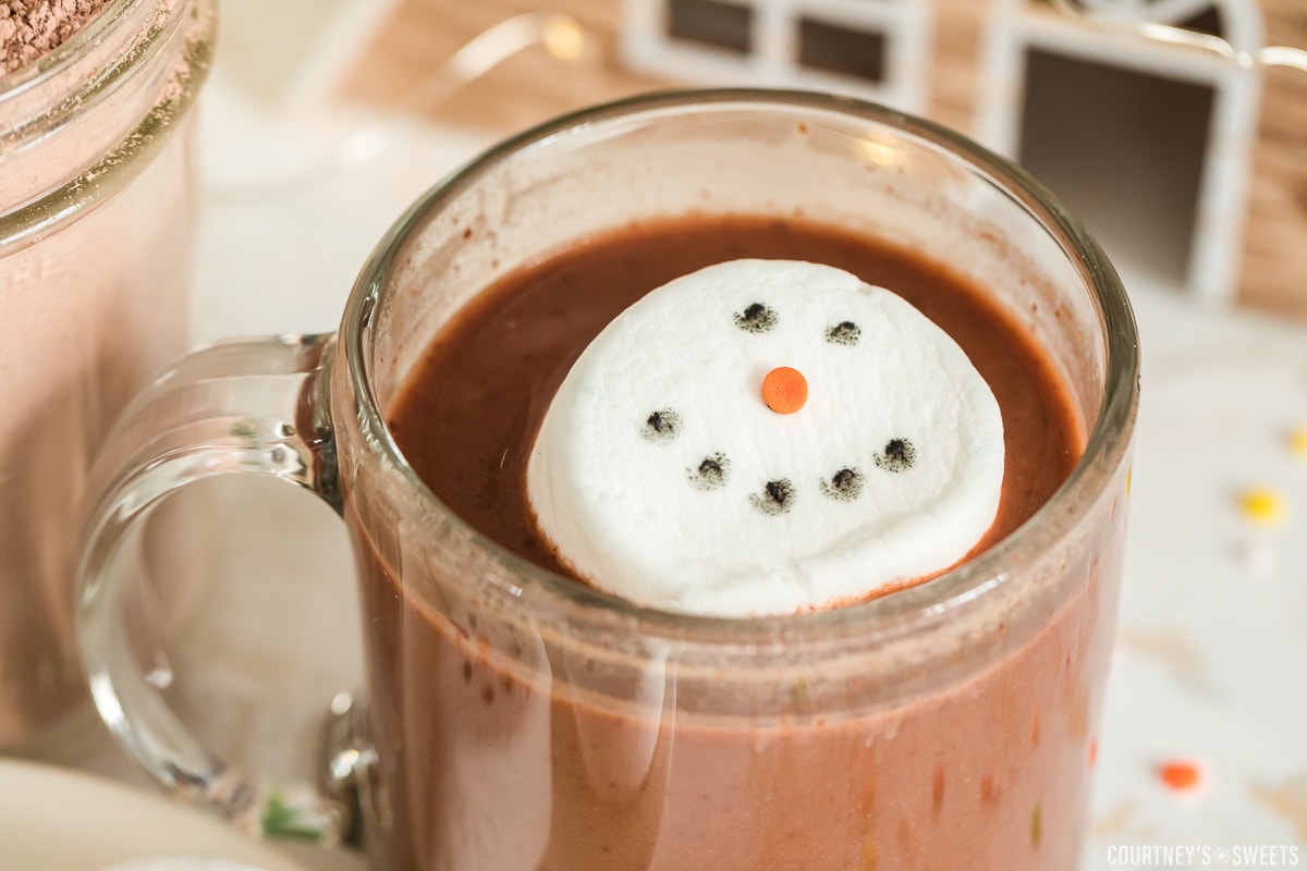 close up of marshmallow decorated as a snowman face in a glass of hot chocolate