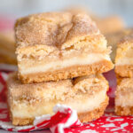 close up snickerdoodle cheesecake bars stacked on a white plate on a red and white napkin with floral print