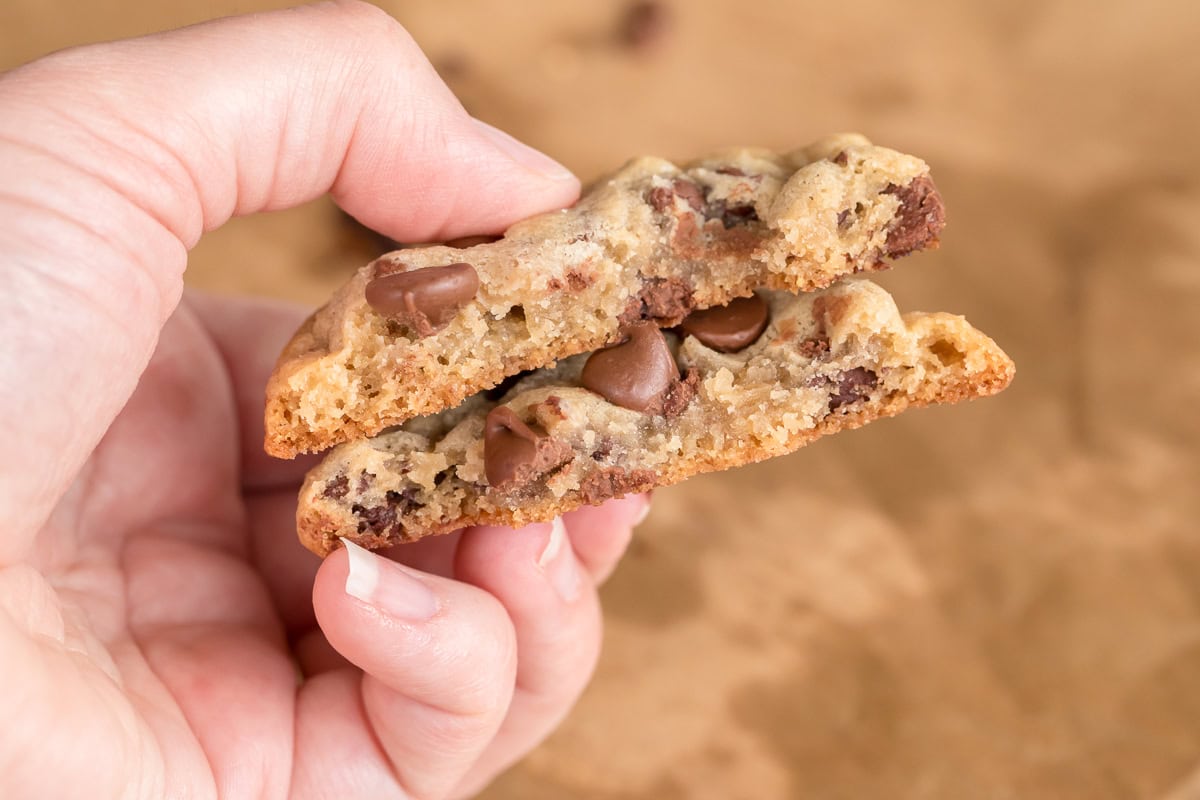 hand holding chocolate chip cookie split in half to show details.
