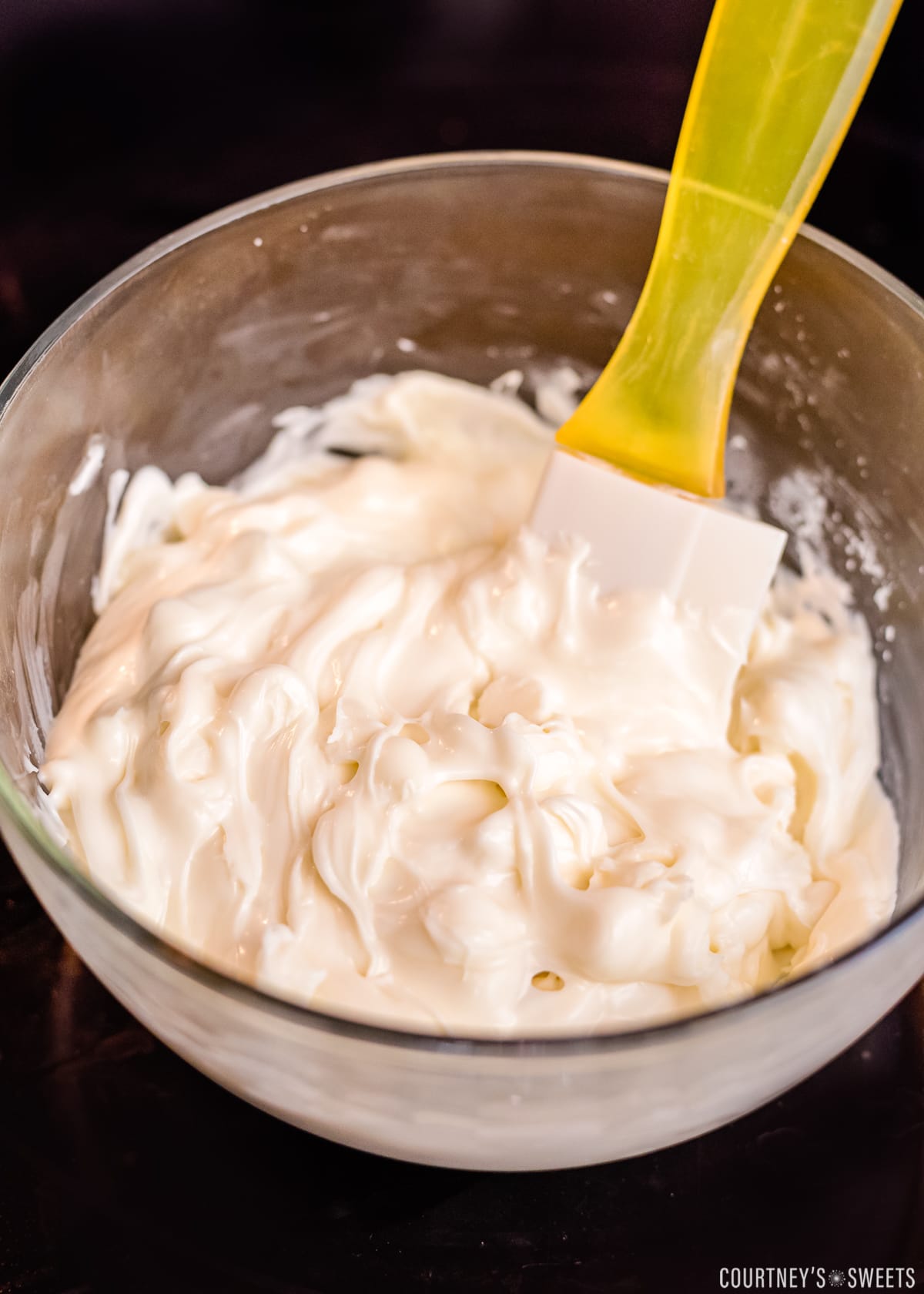 melting white chocolate in a microwave in glass bowl with yellow spatula