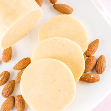 almond paste roll and slices on a white plate with scattered almonds.