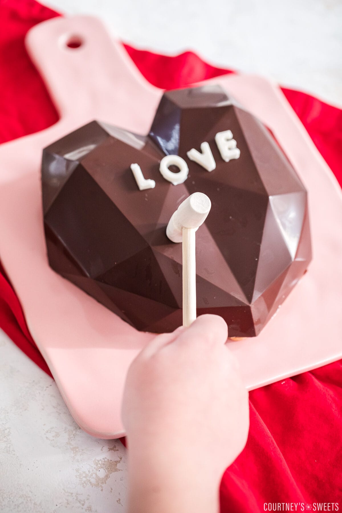 hand holding small wooden hammer over breakable chocolate heart.