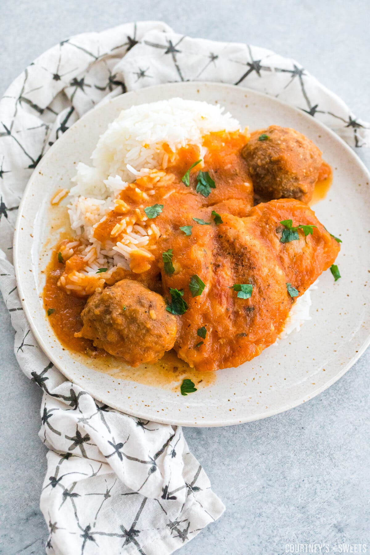 overhead photo of chicken fricassee with meatballs and rice on a plate garnished with chopped parsley.