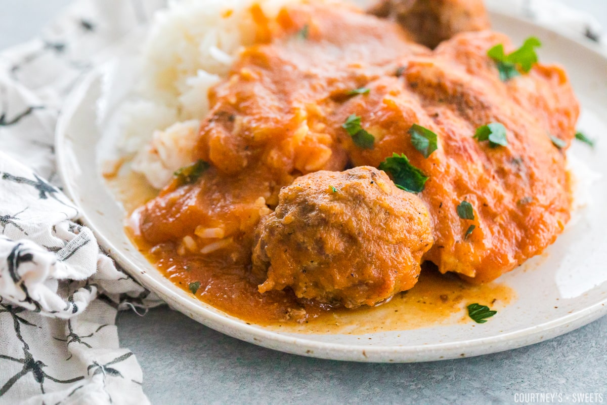  close up of chicken fricassee with meatballs and rice on a plate garnished with chopped parsley.