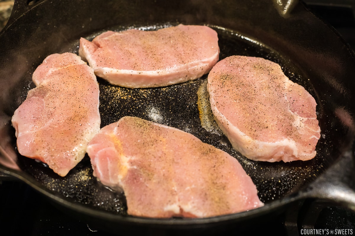 seasoned pork chops searing on a cast iron skillet.