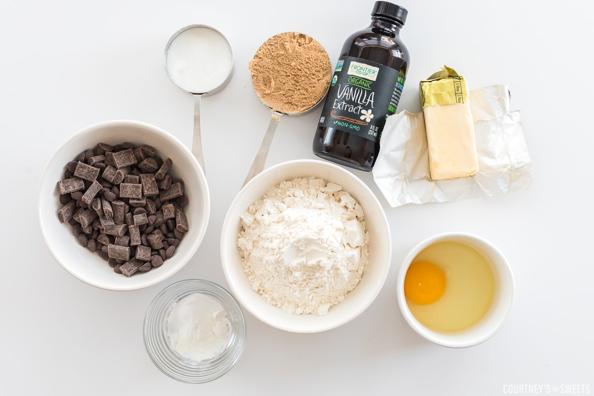 ingredients in bowls and measuring cups for chocolate chip cookies on a white board.