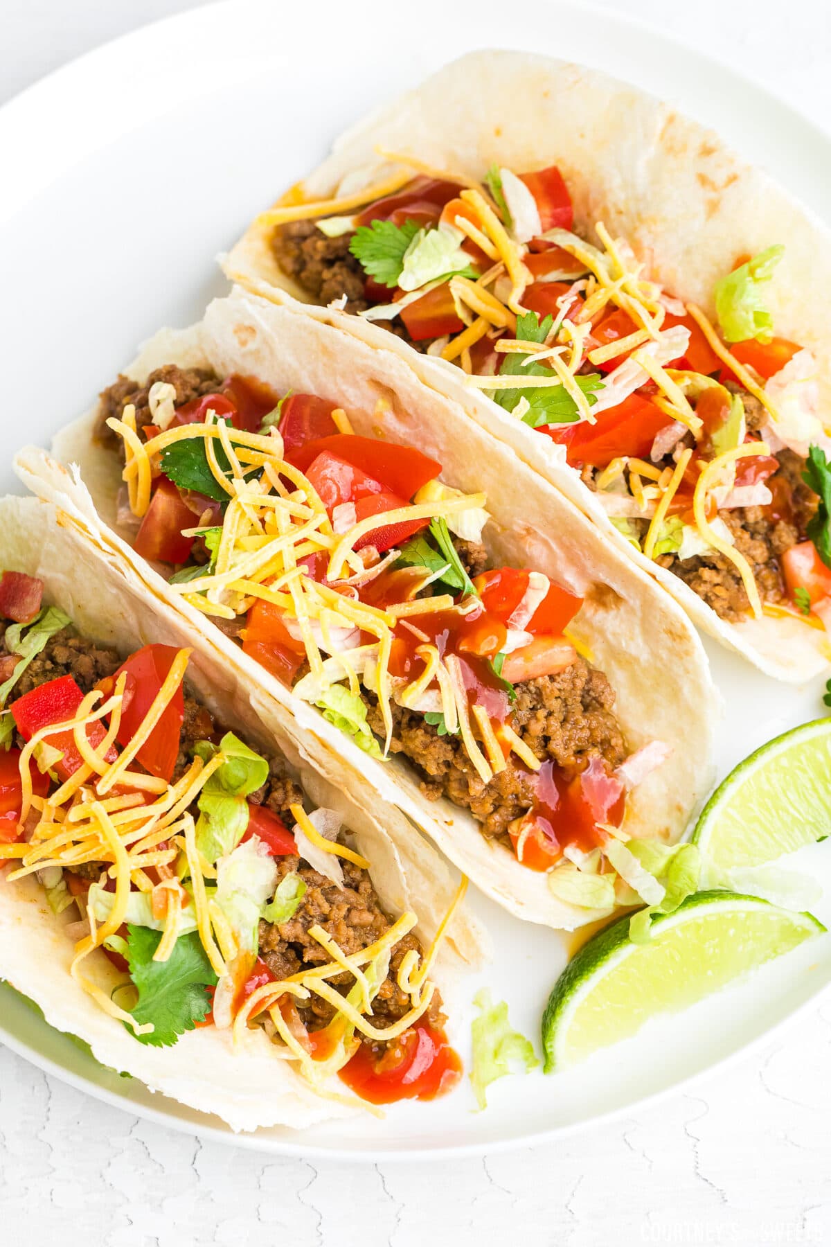 soft ground beef tacos on a white plate with lime wedges