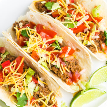 soft ground beef tacos on a white plate with lime wedges