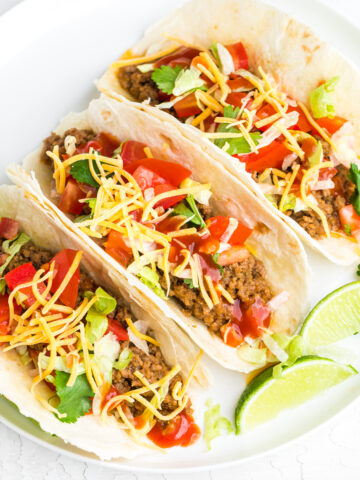 soft ground beef tacos on a white plate with lime wedges