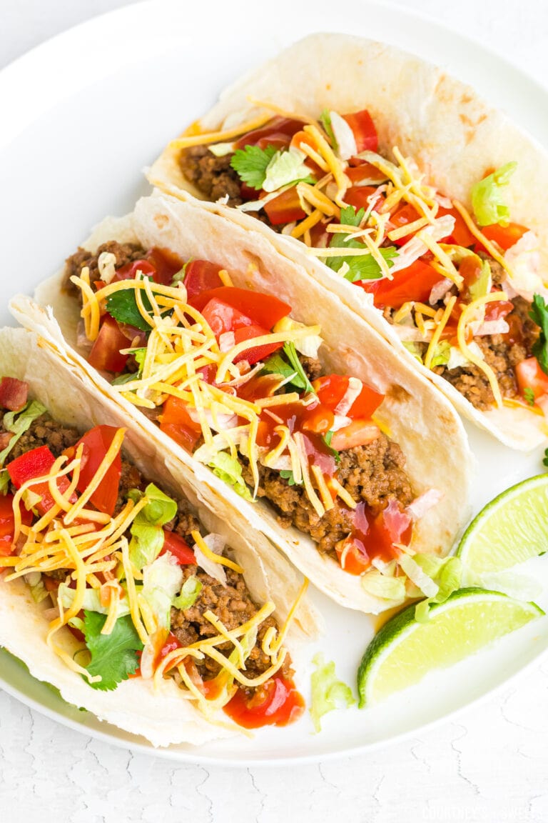soft ground beef tacos on a white plate with lime wedges
