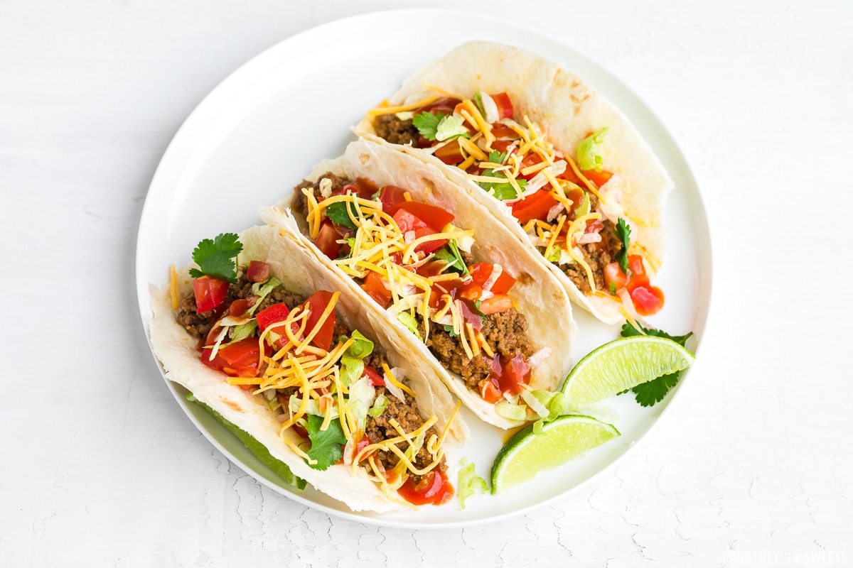 ground beef tacos on a white plate with two lime wedges.