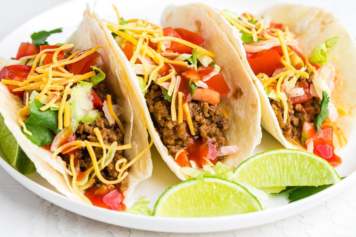 close up of 3 beef tacos on a plate with lime slices.