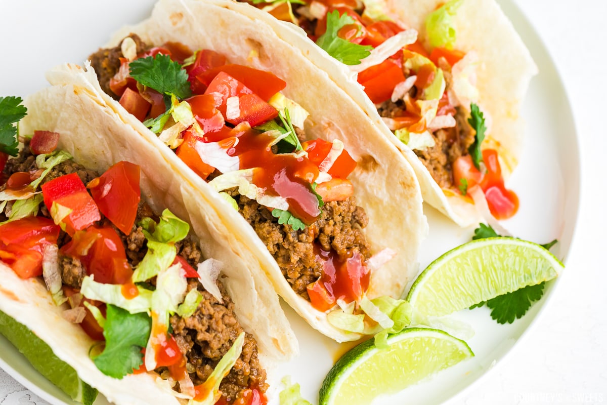 close up of 3 beef tacos on a plate with lime slices.