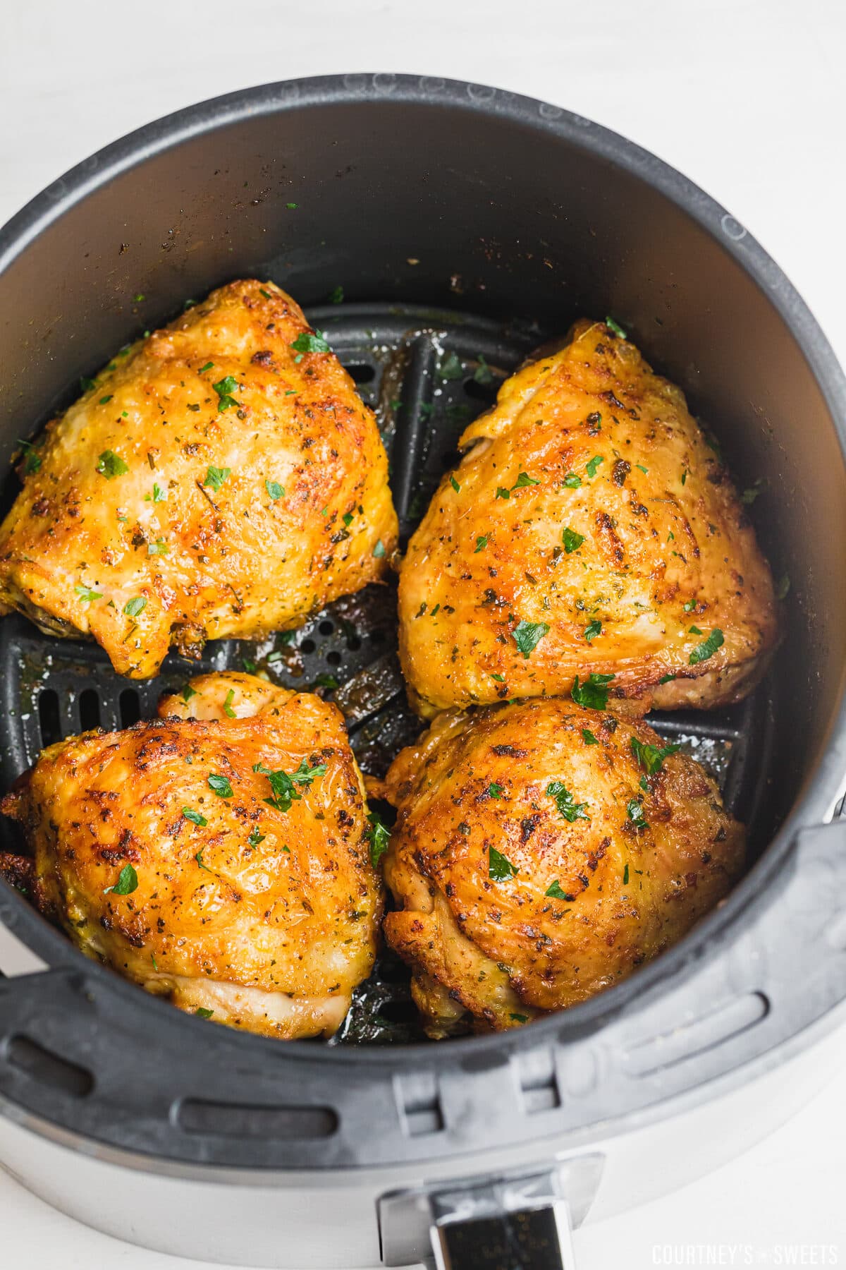 crispy chicken thighs in air fryer basket with parsley garnish.