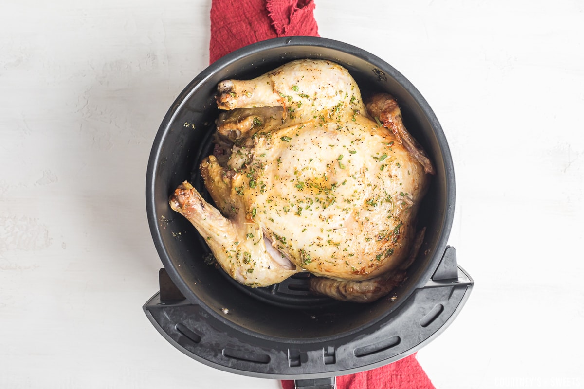 par cooked whole chicken in air fryer basket.