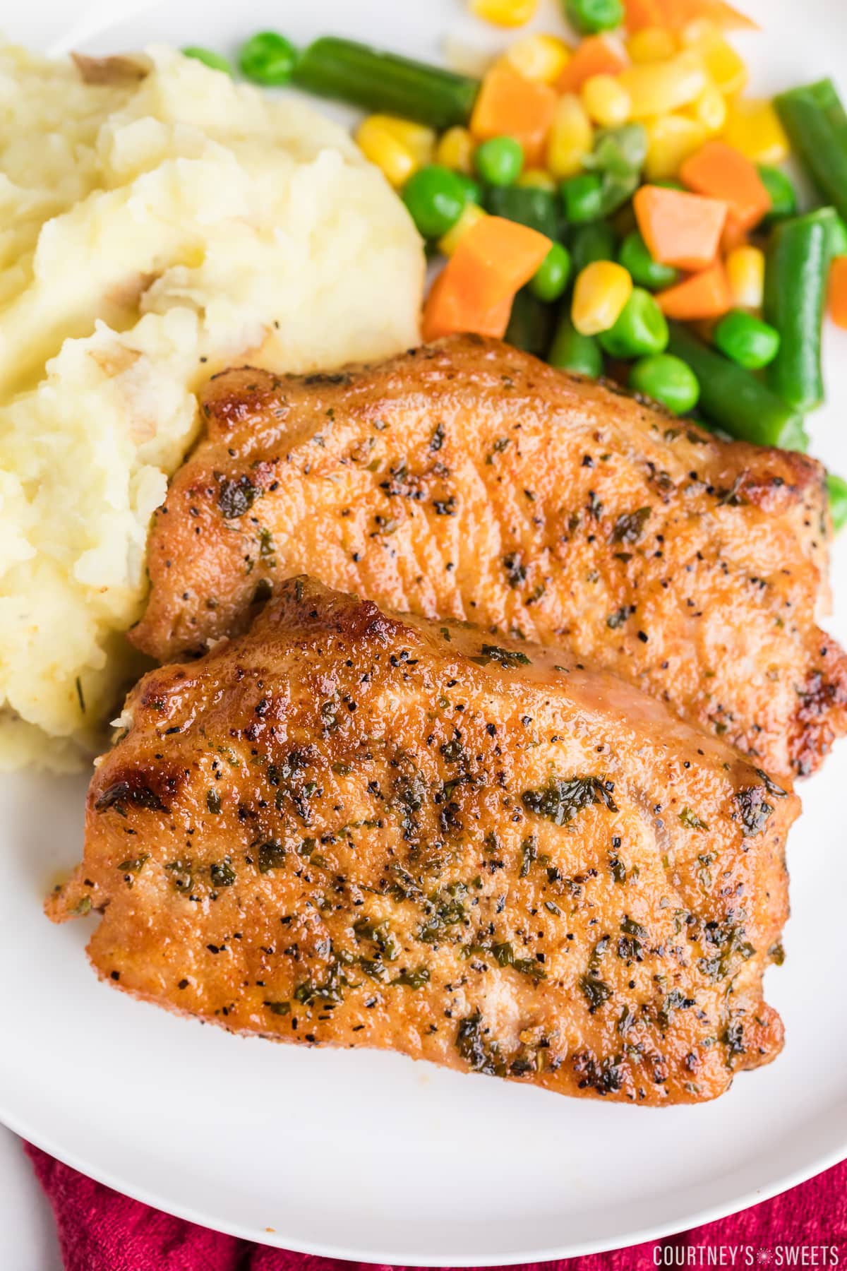 close up of two baked boneless pork chops on a plate with mixed vegetables and mashed potatoes.