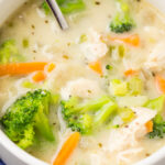 close up of chicken and broccoli soup in a white bowl with a spoon on a navy blue napkin.