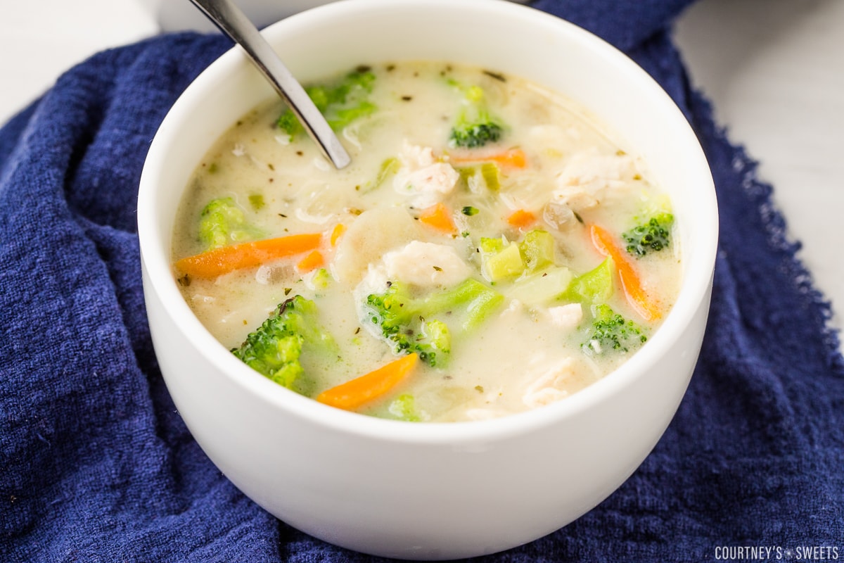 homemade chicken broccoli soup in a white bowl with a spoon on a navy blue cloth napkin.