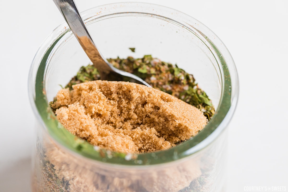 brown sugar on top of seasoning blend in a glass jar with spoon.