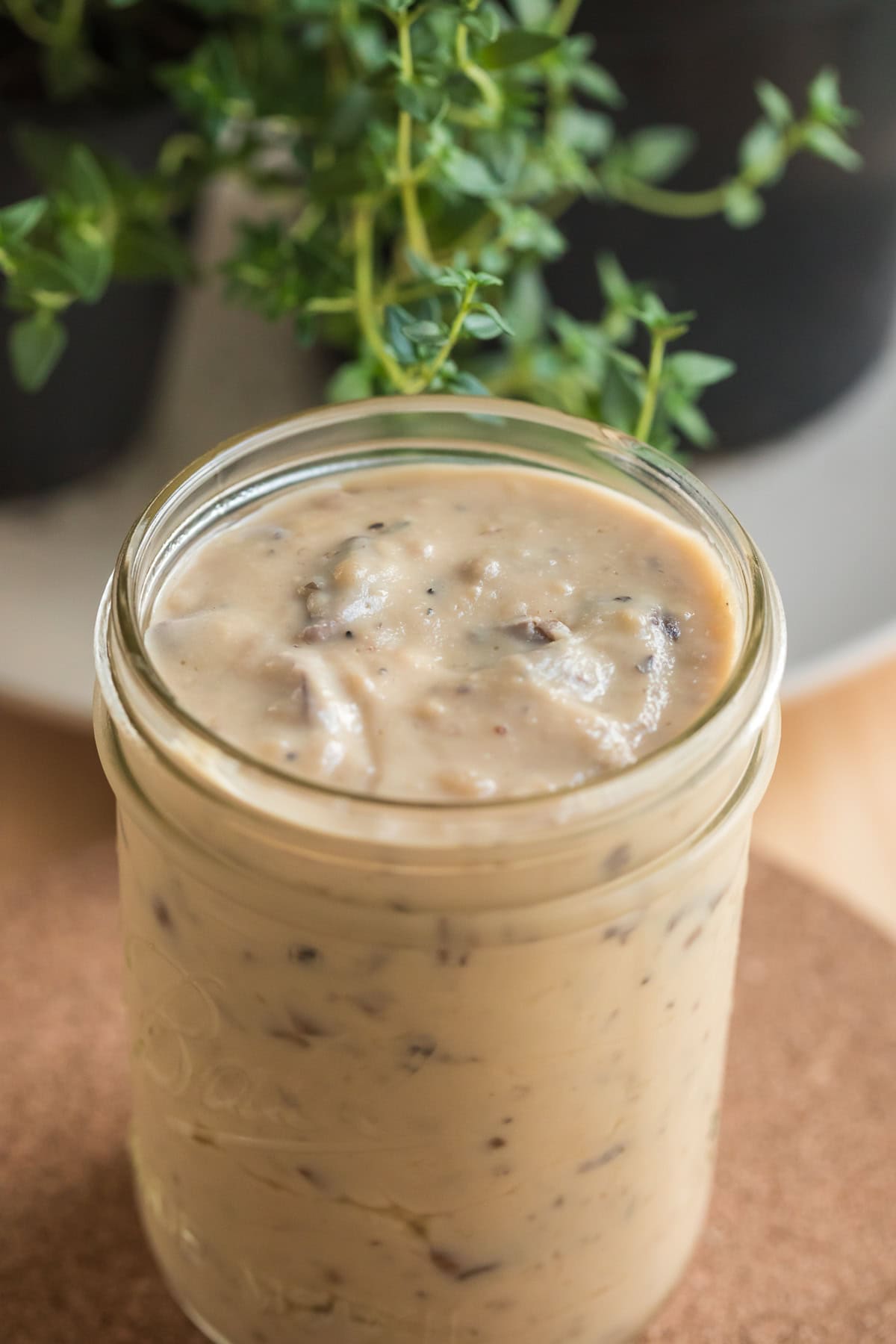 From-scratch condensed cream of mushroom soup in a mason jar with fresh herbs in the background.