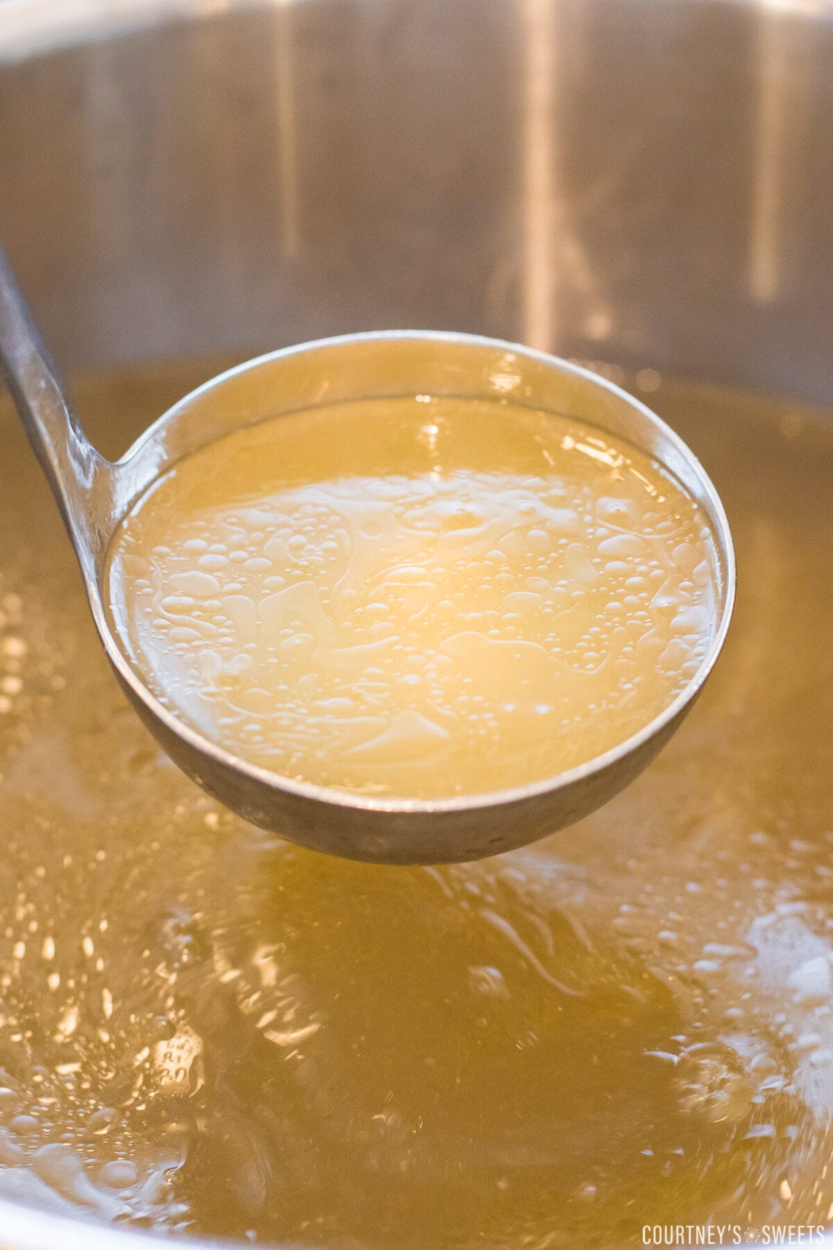 ladle showing chicken broth in a big pot of chicken broth.