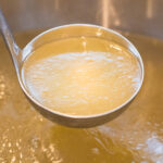 ladle showing chicken broth in a big pot of chicken broth.
