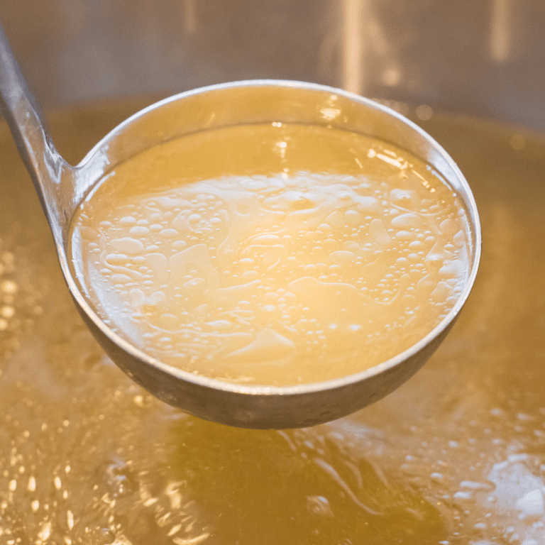 homemade chicken broth on soup ladle in a stockpot.
