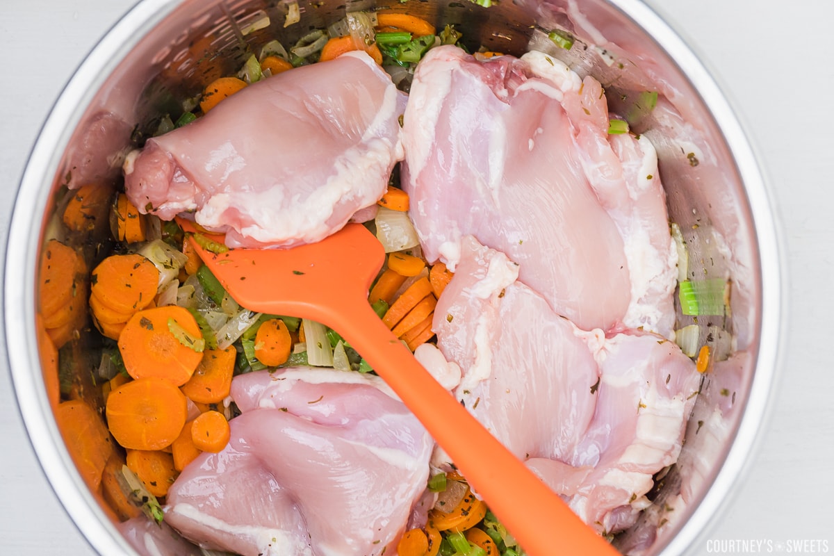 boneless skinless chicken thighs on top of cooked vegetables for soup in instant pot bowl with a spatula inside.