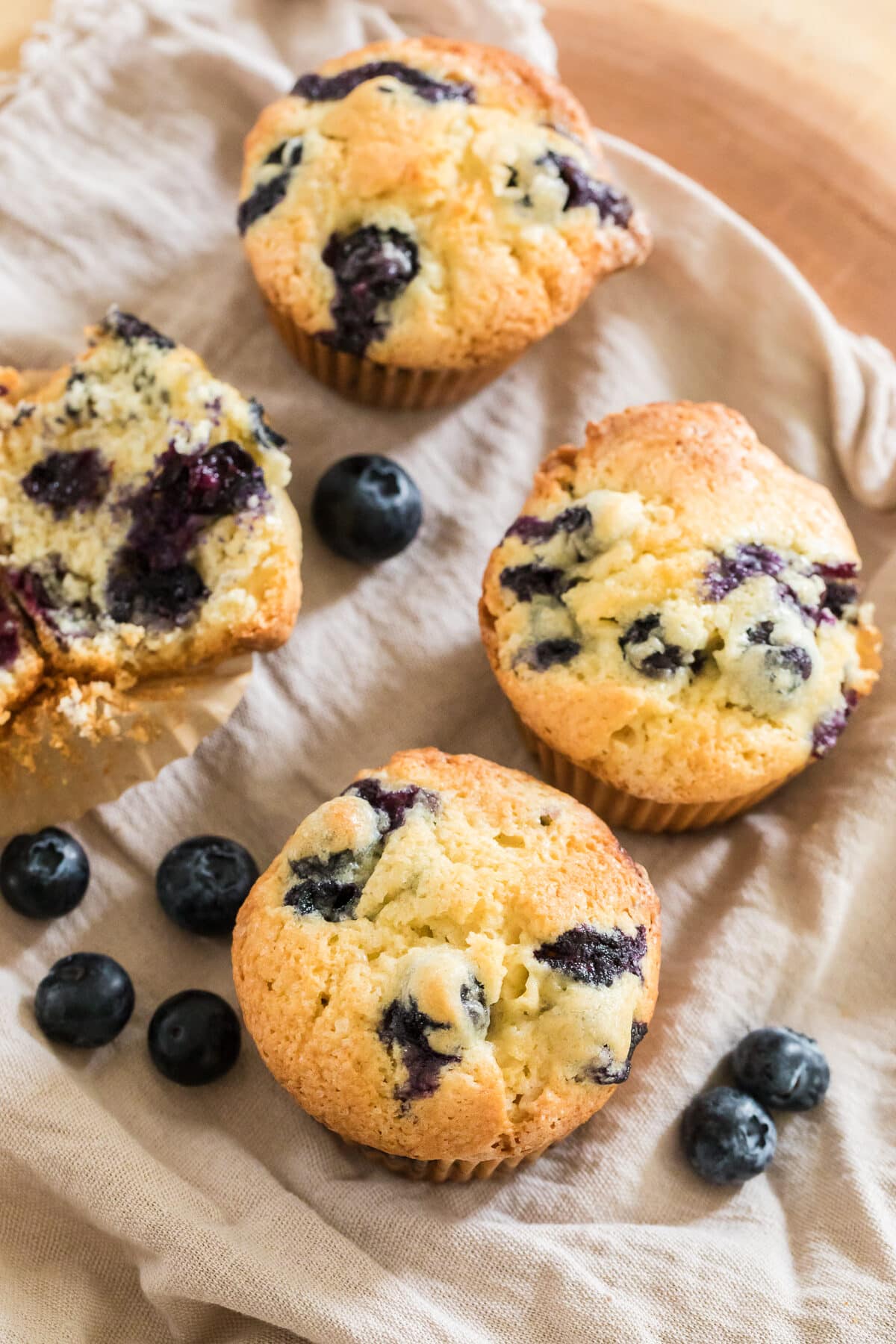 blueberry muffins on a beige napkin with blueberries scattered.
