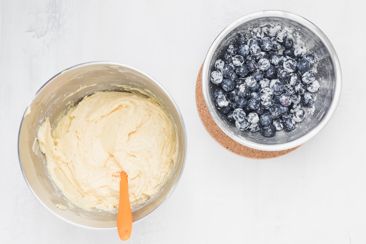 muffin batter in a bowl to the left and floured blueberries to the right.