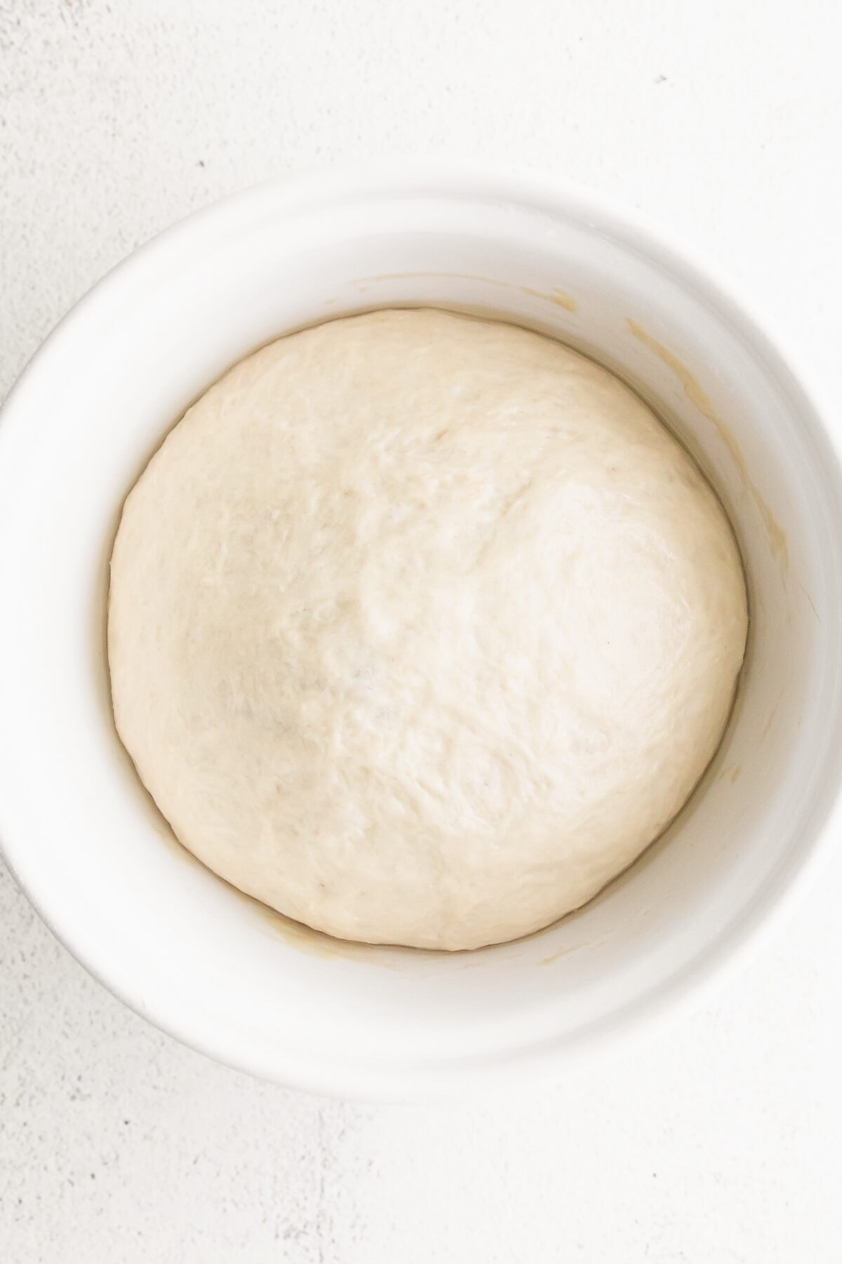 Risen bagel dough in a white bowl.