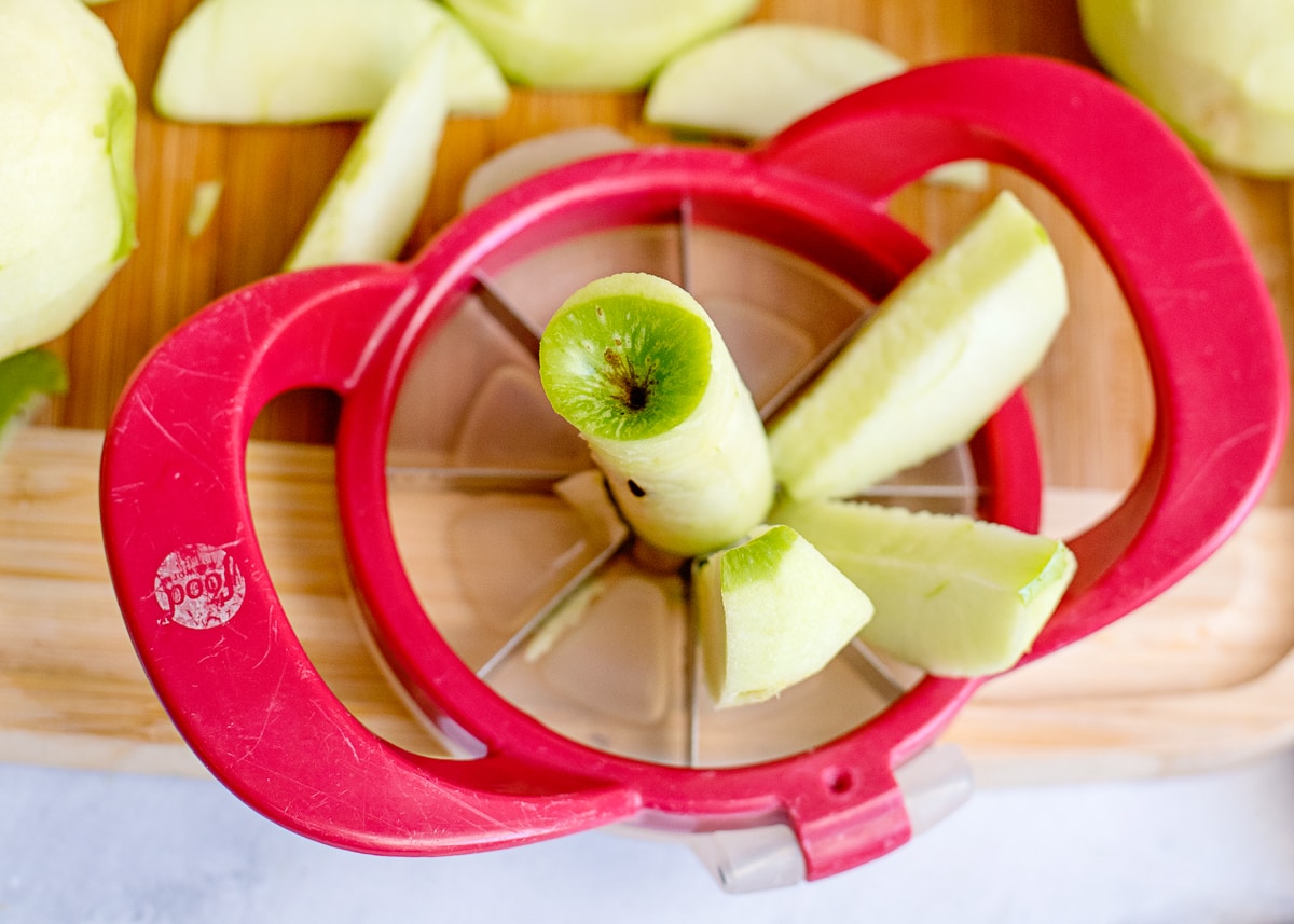 red apple corer with a core and 3 slices on a cutting board.
