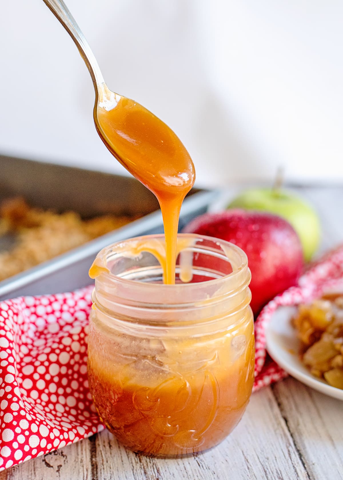 spoon drizzling caramel sauce into a glass jar.