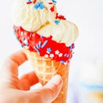 hand holding fourth of july chocolate dipped cone with red chocolate layer with sprinkles and ice cream.