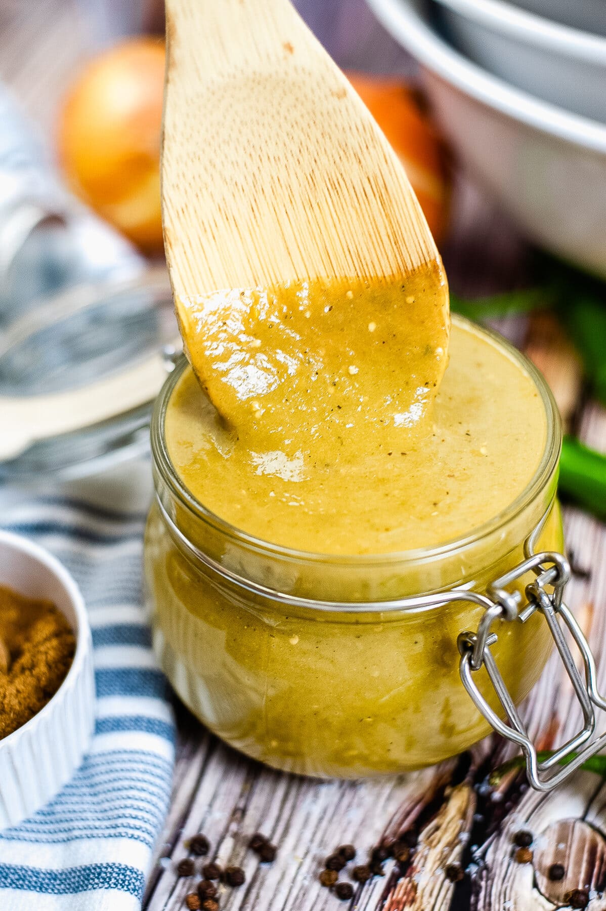 wooden spoon dipping into green enchilada sauce in a glass jar.