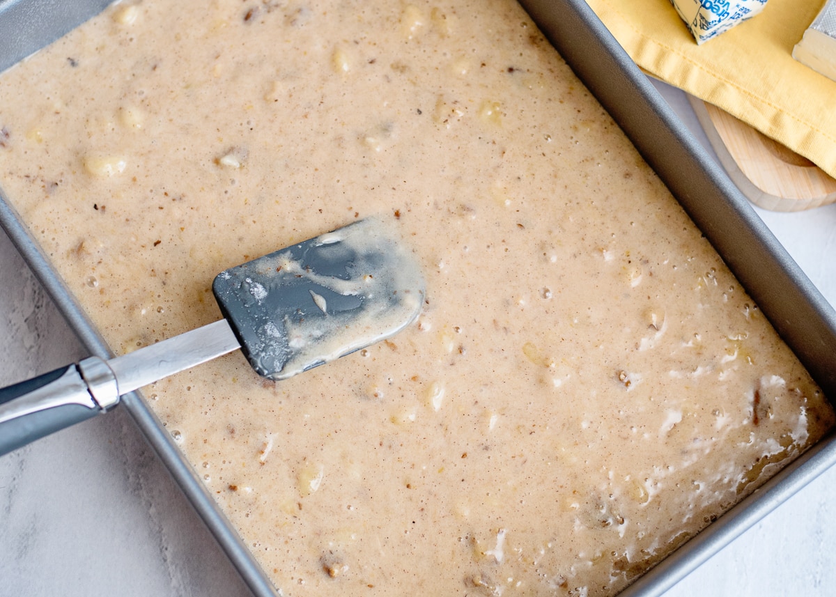 banana nut cake batter in a rectangle cake pan with a spatula on top to spread.