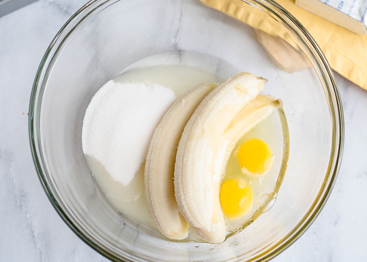 bananas, oil, sugar, and eggs, in a bowl.