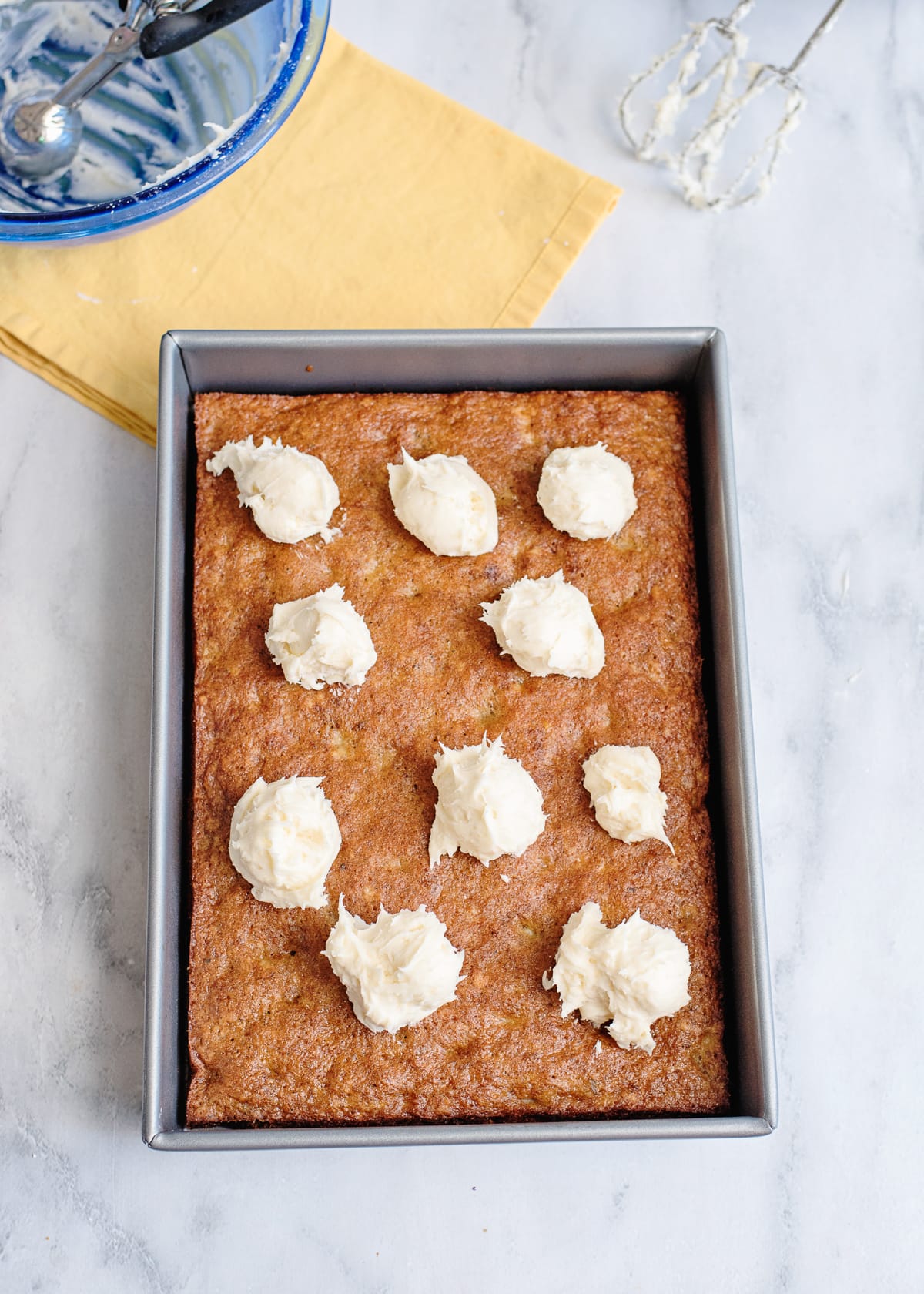 cooked banana nut cake in a baking dish with dollops of frosting on it ready to spread.