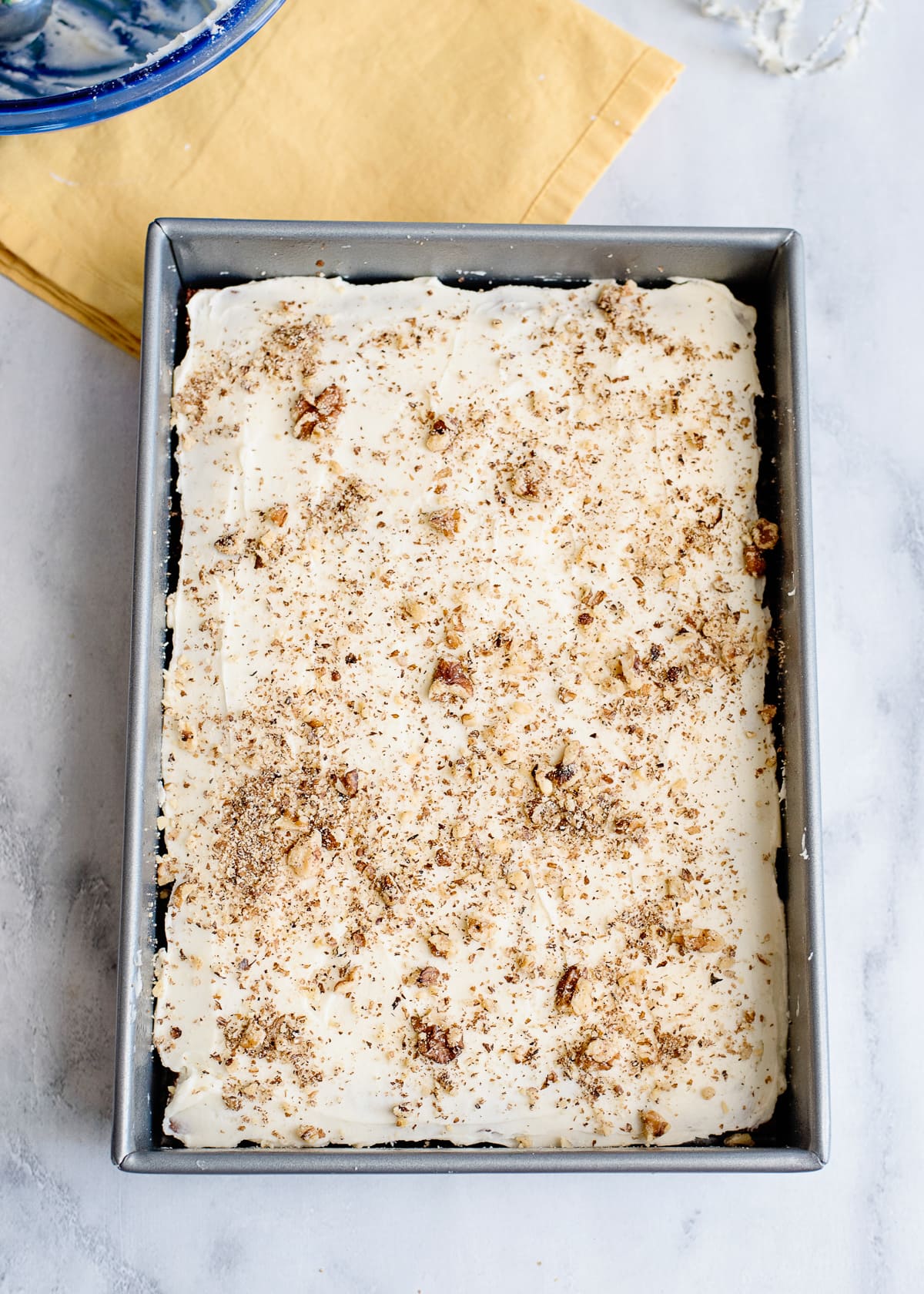 cooked banana nut cake in a baking dish with dollops of frosting and crushed walnuts.